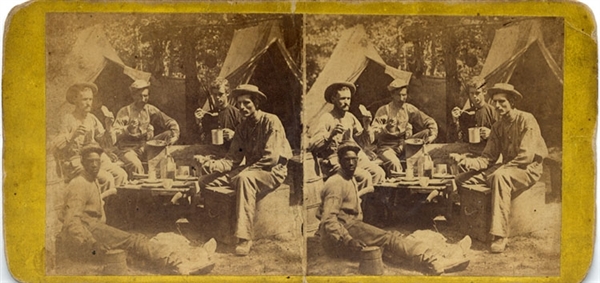 A terrific close-up of five men including an African American dining in camp